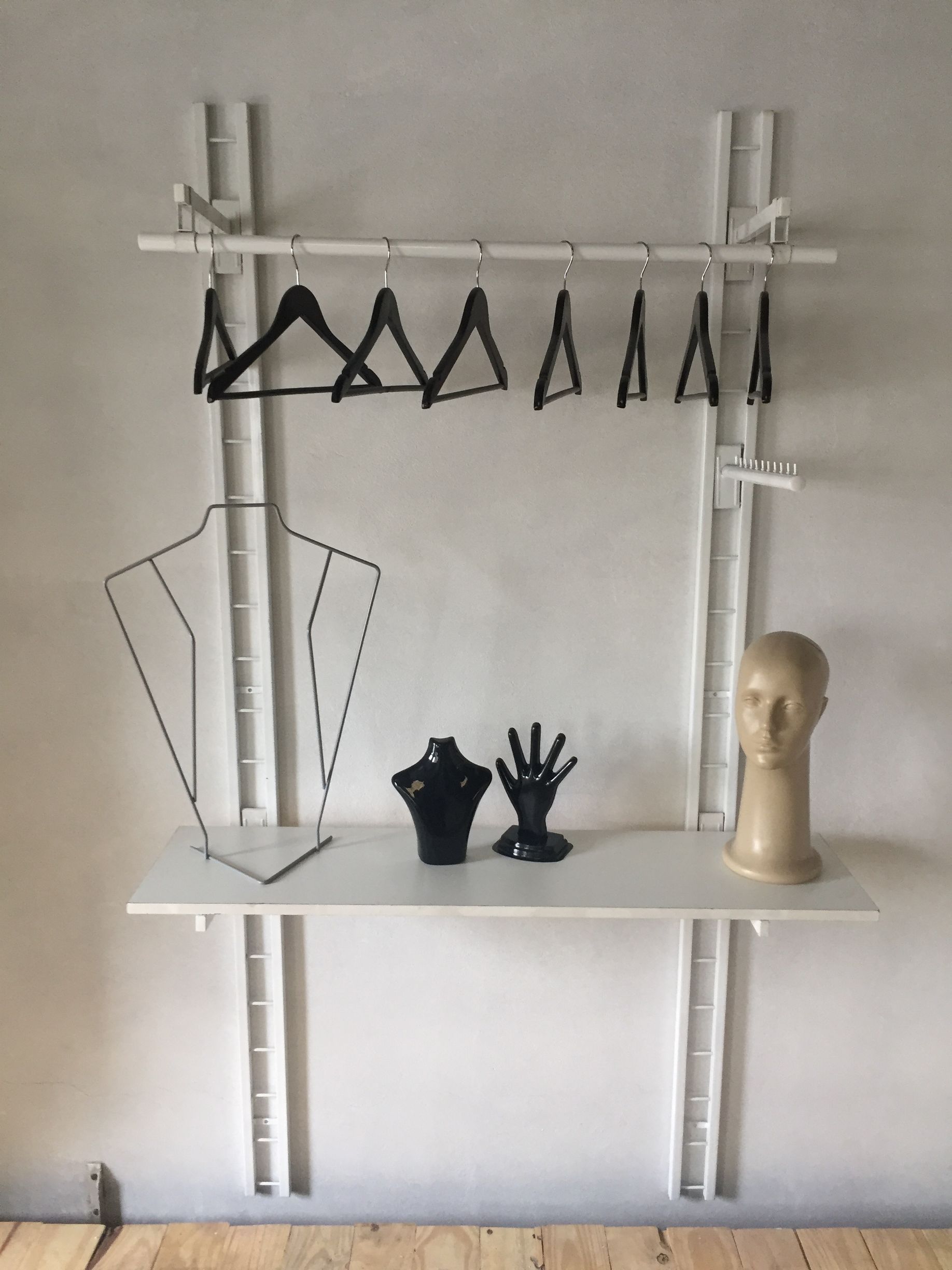 Perchero de pared de color blanco con perchas negras y un estante que sostiene un busto de maniquí, una mano y una cabeza.