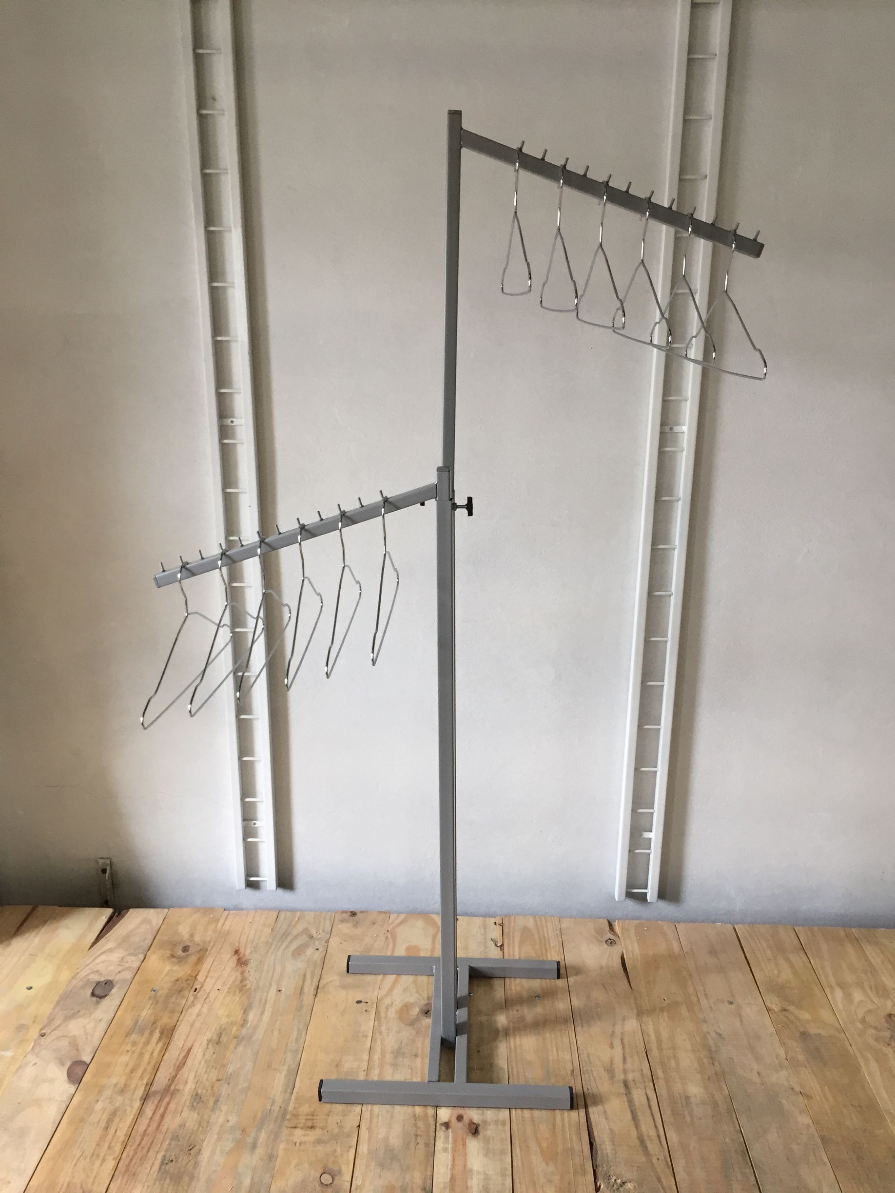 Un perchero con perchas se encuentra sobre un piso de madera contra una pared blanca.
