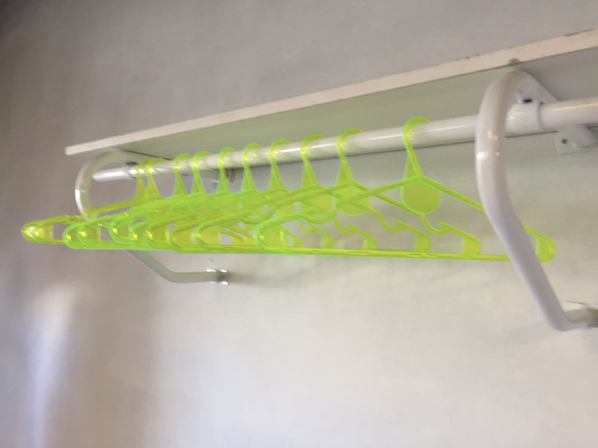 Perchas de plástico verde colgadas en un estante blanco fijado a una pared.