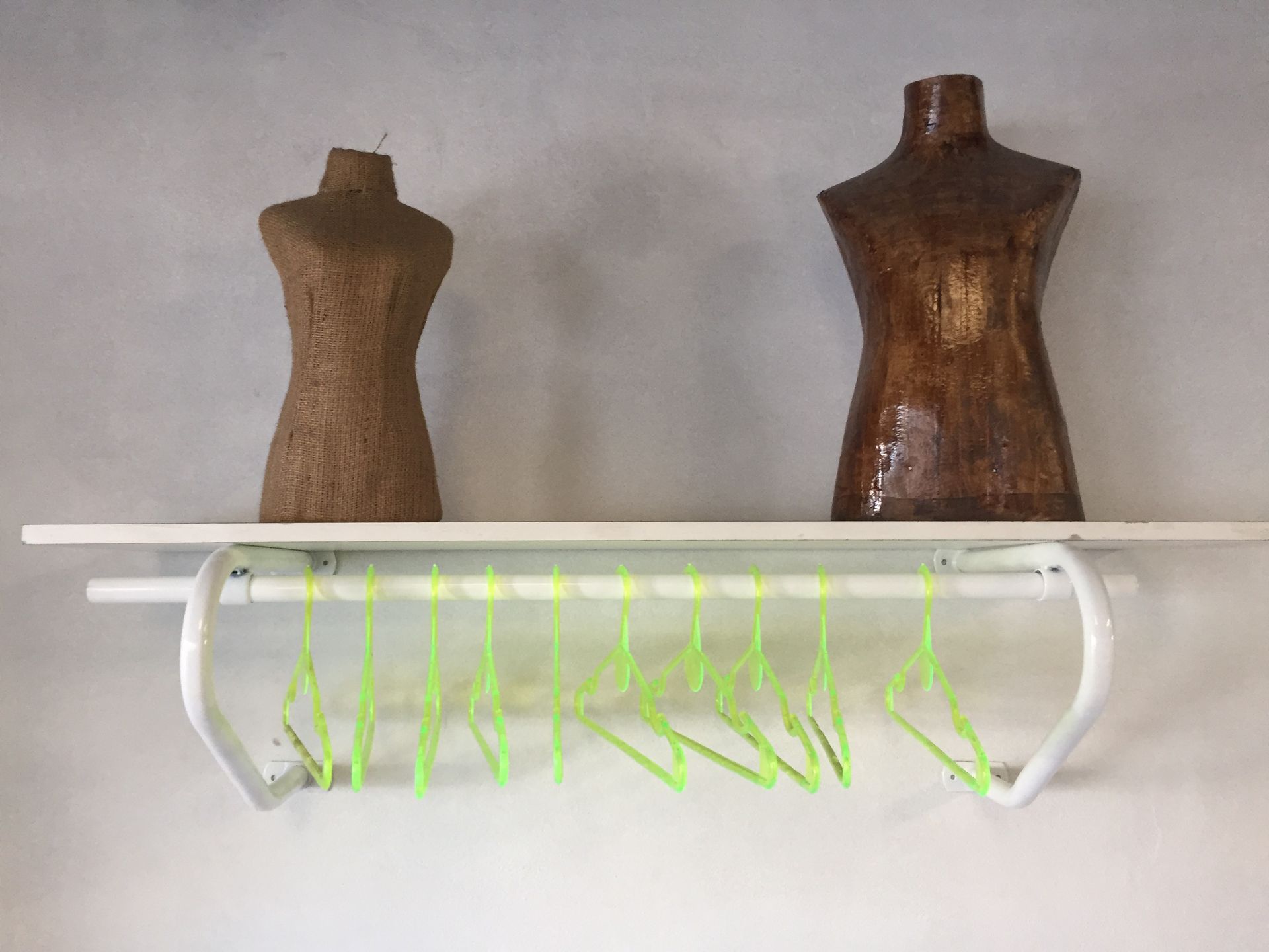 Dos maniquíes marrones en un estante blanco encima de una barra blanca con perchas verdes.