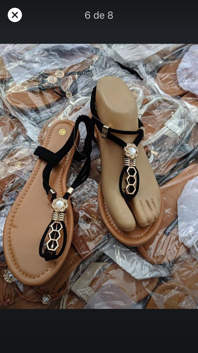 Sandalias con tiras negras, cuentas decorativas y suela color canela. Una de ellas está sobre una horma de pie.