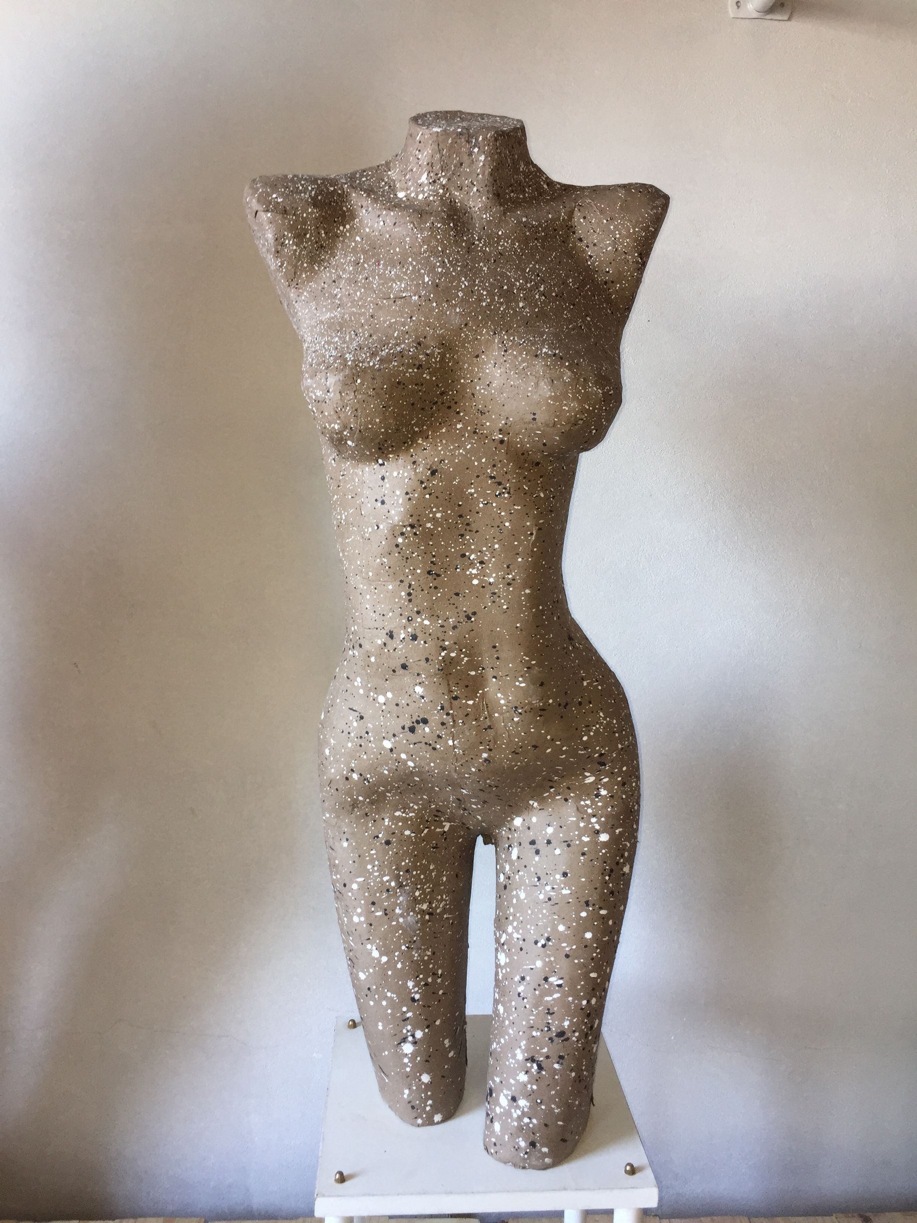 Torso de maniquí cubierto de purpurina plateada y negra, de pie sobre una plataforma blanca.