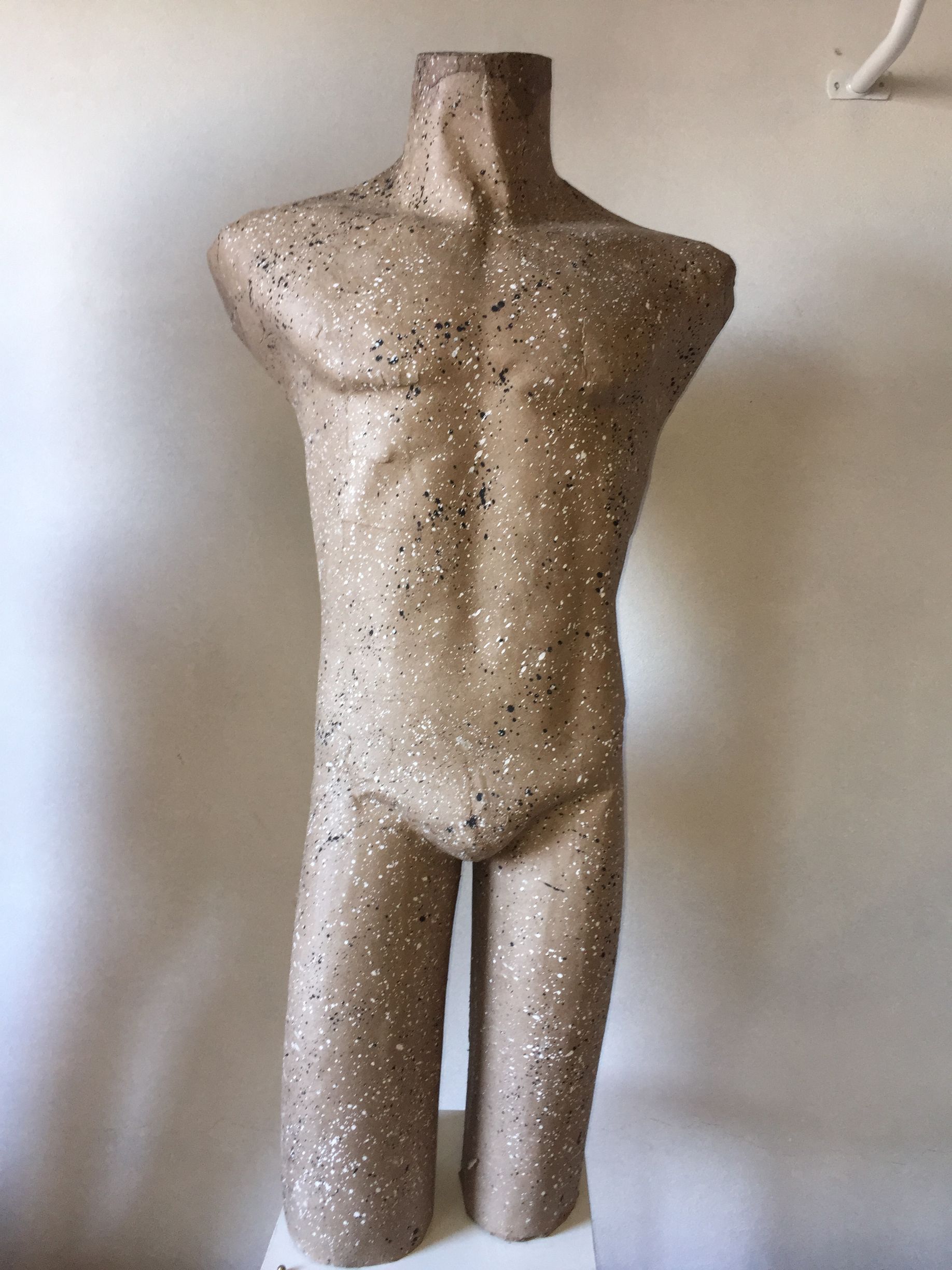 Torso de maniquí, de color canela con manchas blancas y negras, de pie frente a una pared beige.