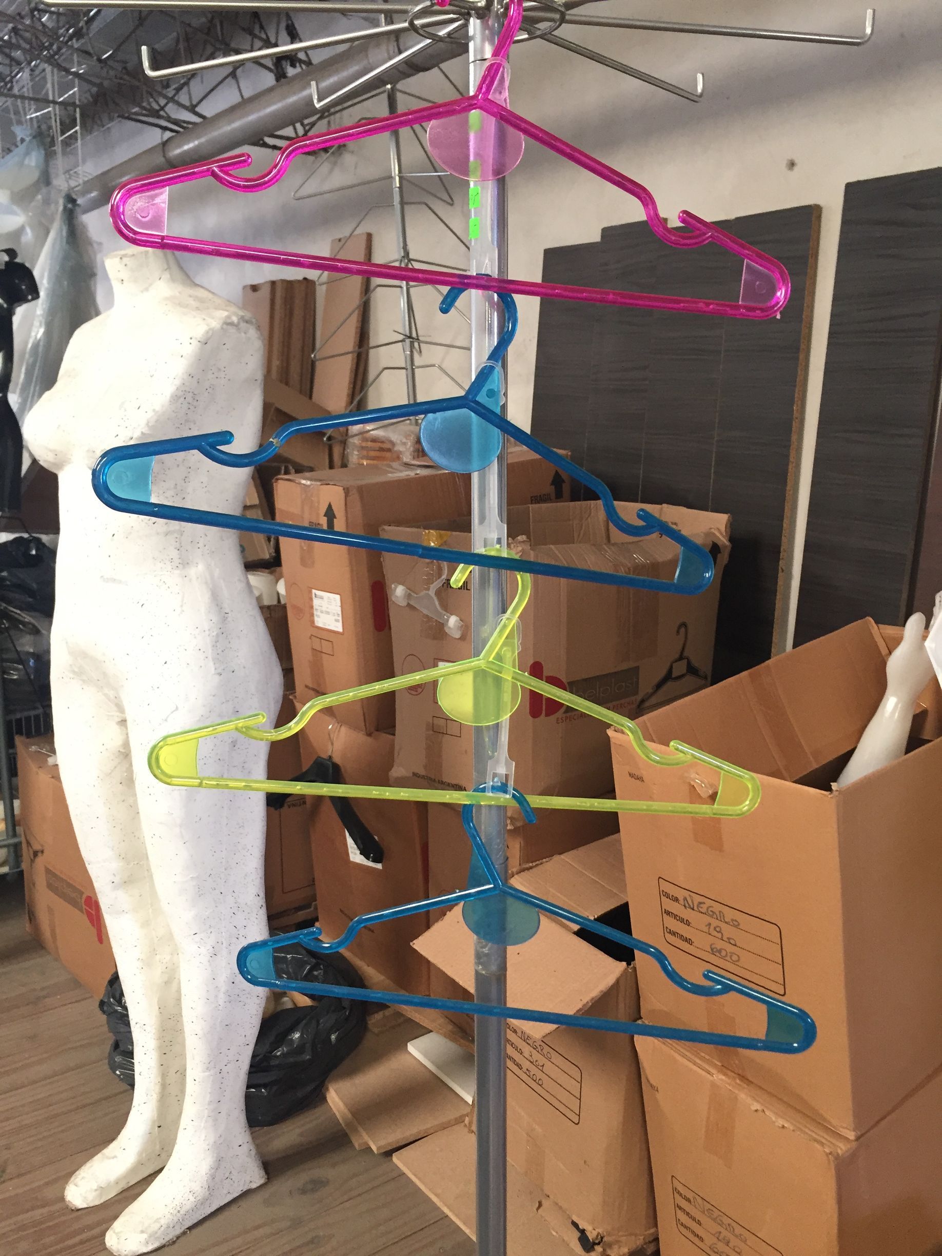 Un expositor de ropa con perchas rosas, azules y verdes; cerca hay un maniquí.