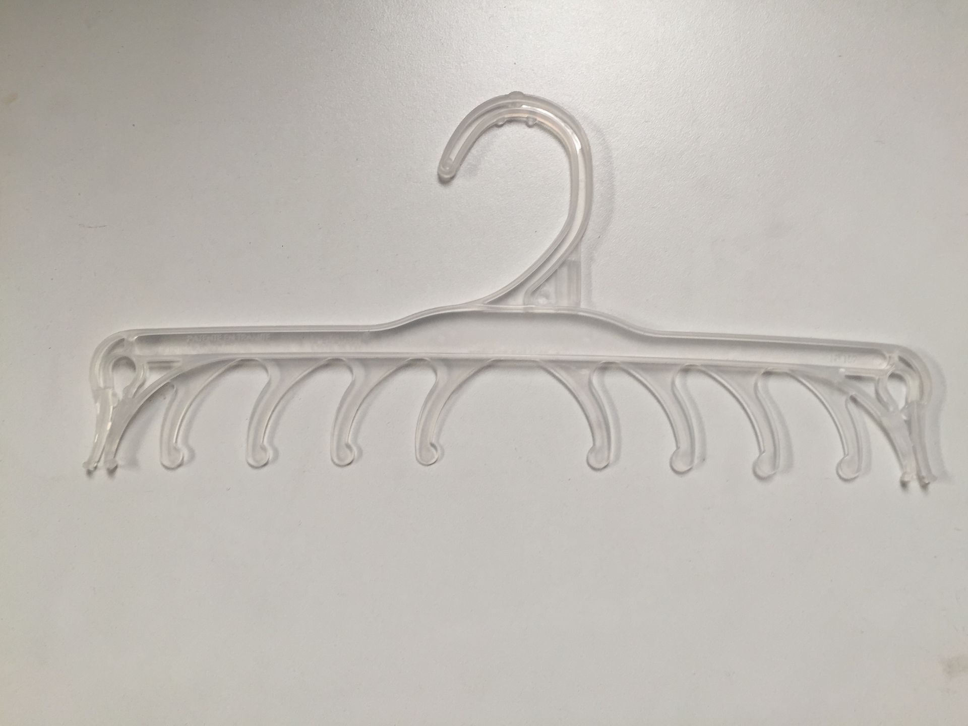 Percha de ropa de plástico transparente con múltiples muescas curvas para colgar artículos.