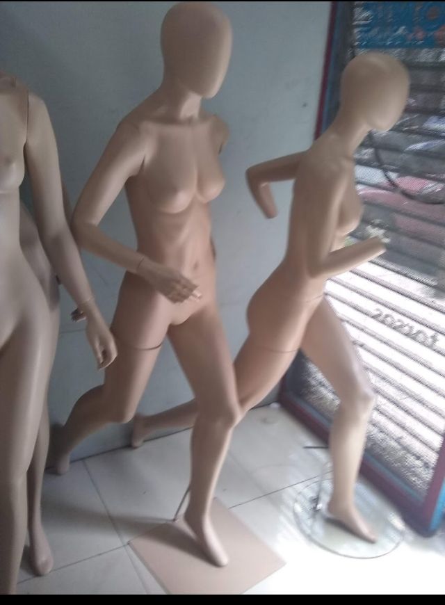 Maniquíes en un escaparate, en posición de correr. Son beige, en un interior con suelo de baldosas.