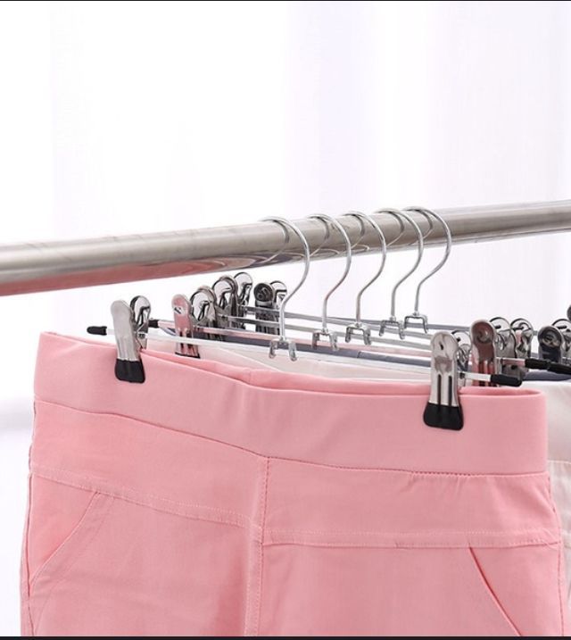 Perchas con pinzas que sostienen pantalones rosas y blancos en una varilla de metal.