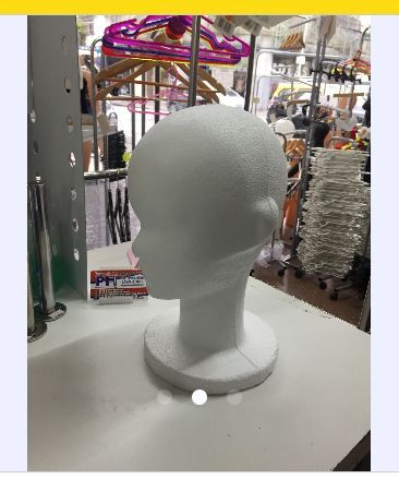 Cabeza de maniquí de espuma blanca sobre una superficie blanca, dentro de una tienda con otros artículos.