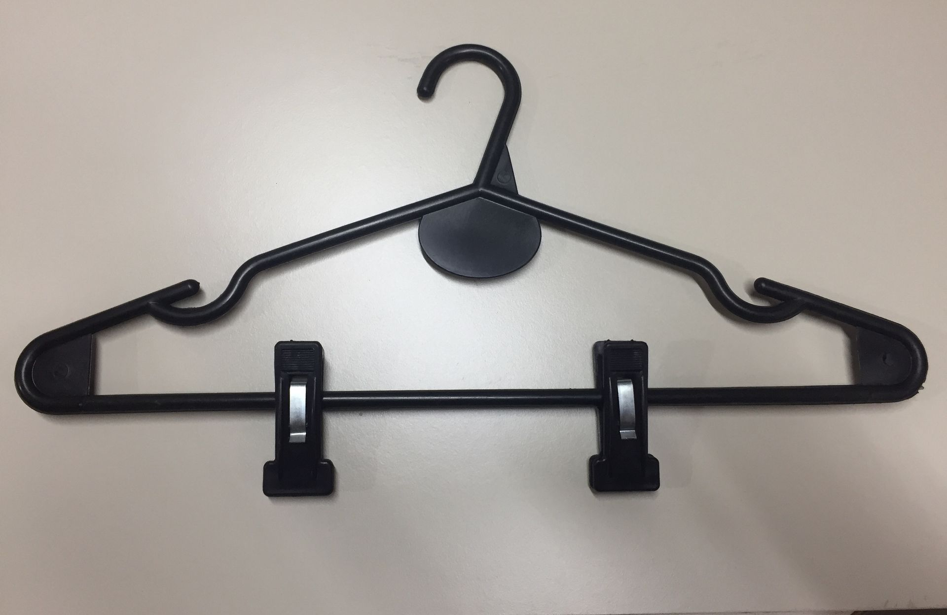 Percha de ropa de plástico negro con pinzas sobre superficie clara.