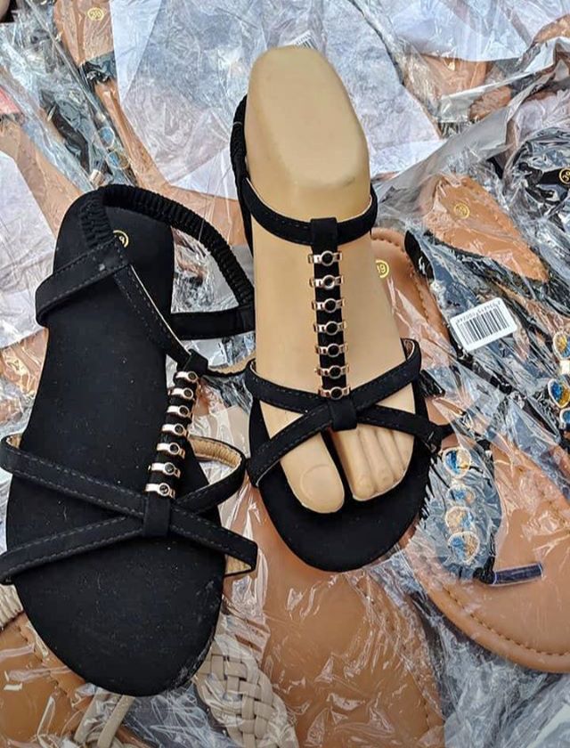 Sandalias negras con detalles plateados, exhibidas sobre una superficie cubierta de plástico con un maniquí de pie.