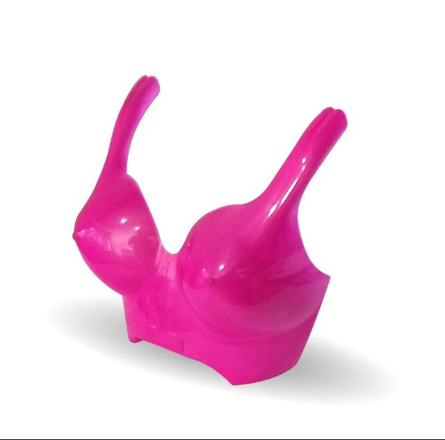 Regadera de plástico de color rosa con forma de sujetador, con un pico largo a cada lado y sobre un fondo blanco.