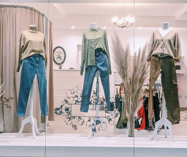 Escaparate de tienda de ropa con maniquíes en tops, vaqueros y pantalones de color beige y verde.