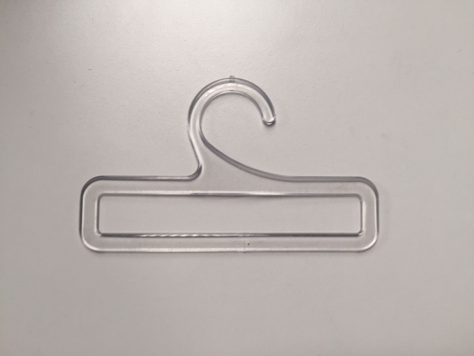 Percha de plástico transparente, con cierre de bucle en la parte superior y base rectangular.