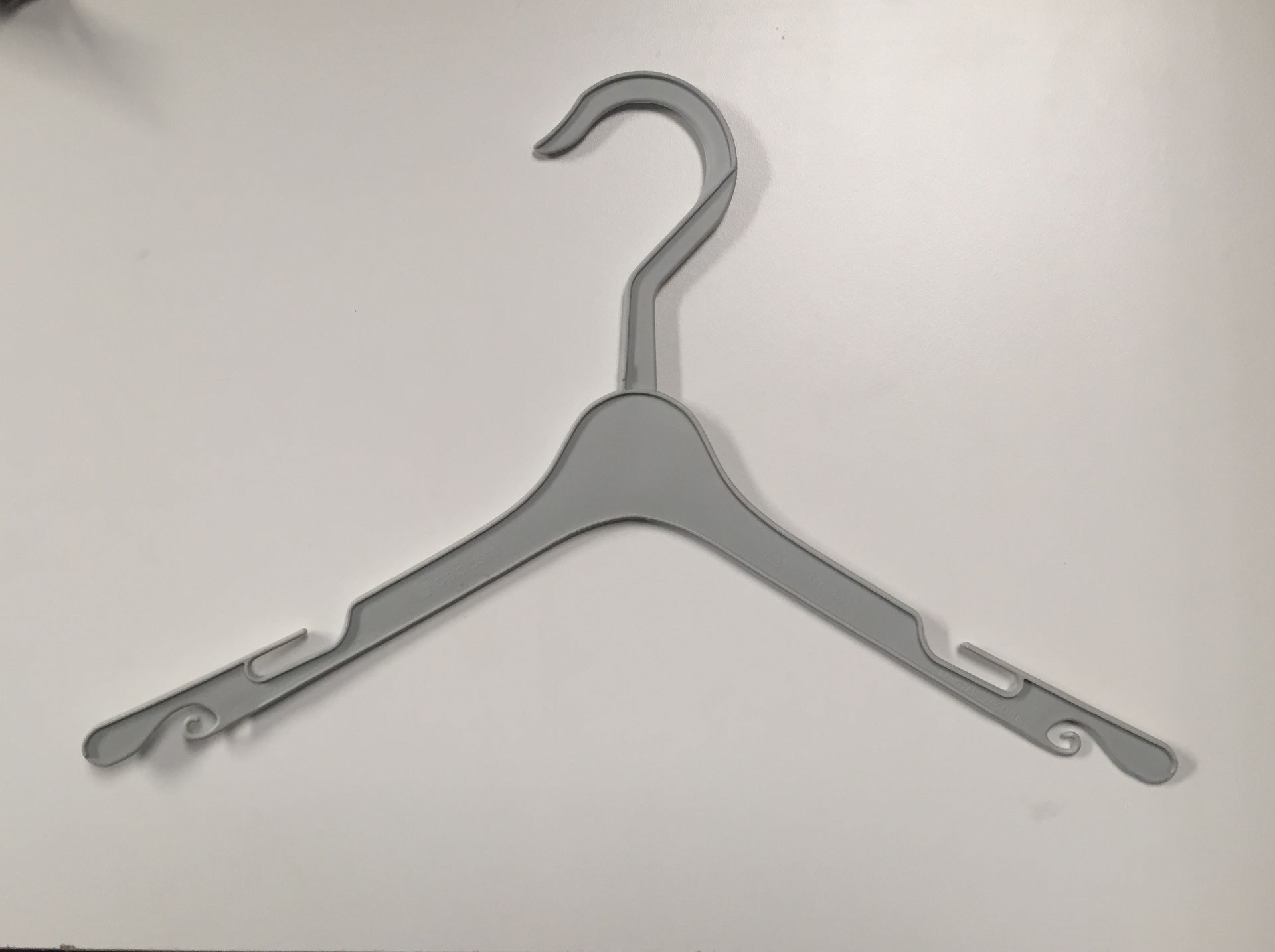 Percha de ropa de plástico gris sobre superficie blanca, con muescas para correas en cada brazo.