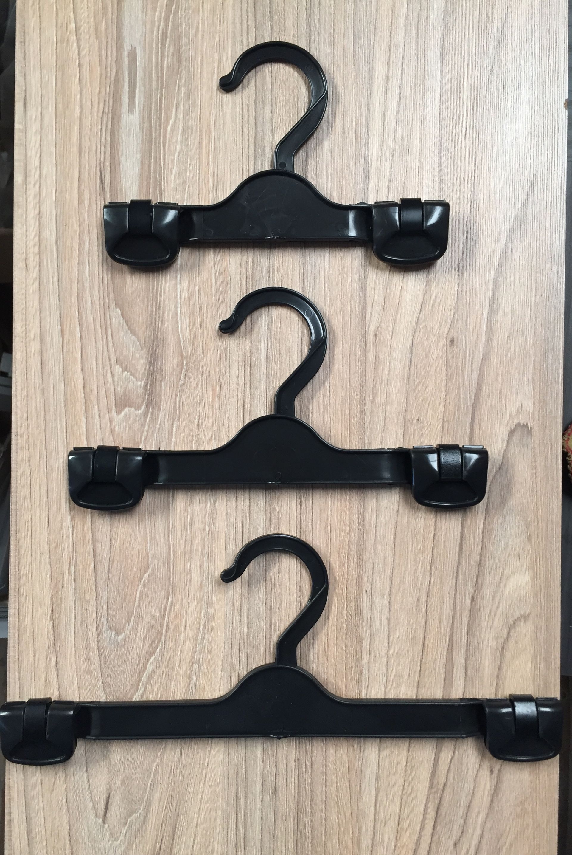 Tres perchas de falda de plástico negro sobre un fondo con vetas de madera.