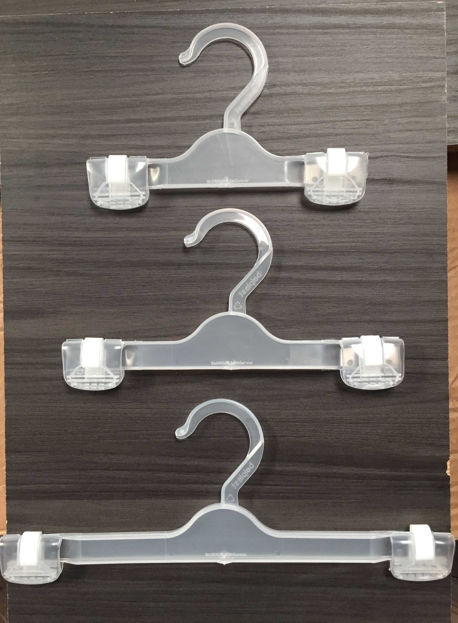 Tres perchas de ropa de plástico transparente con clips, sobre una superficie de madera oscura.