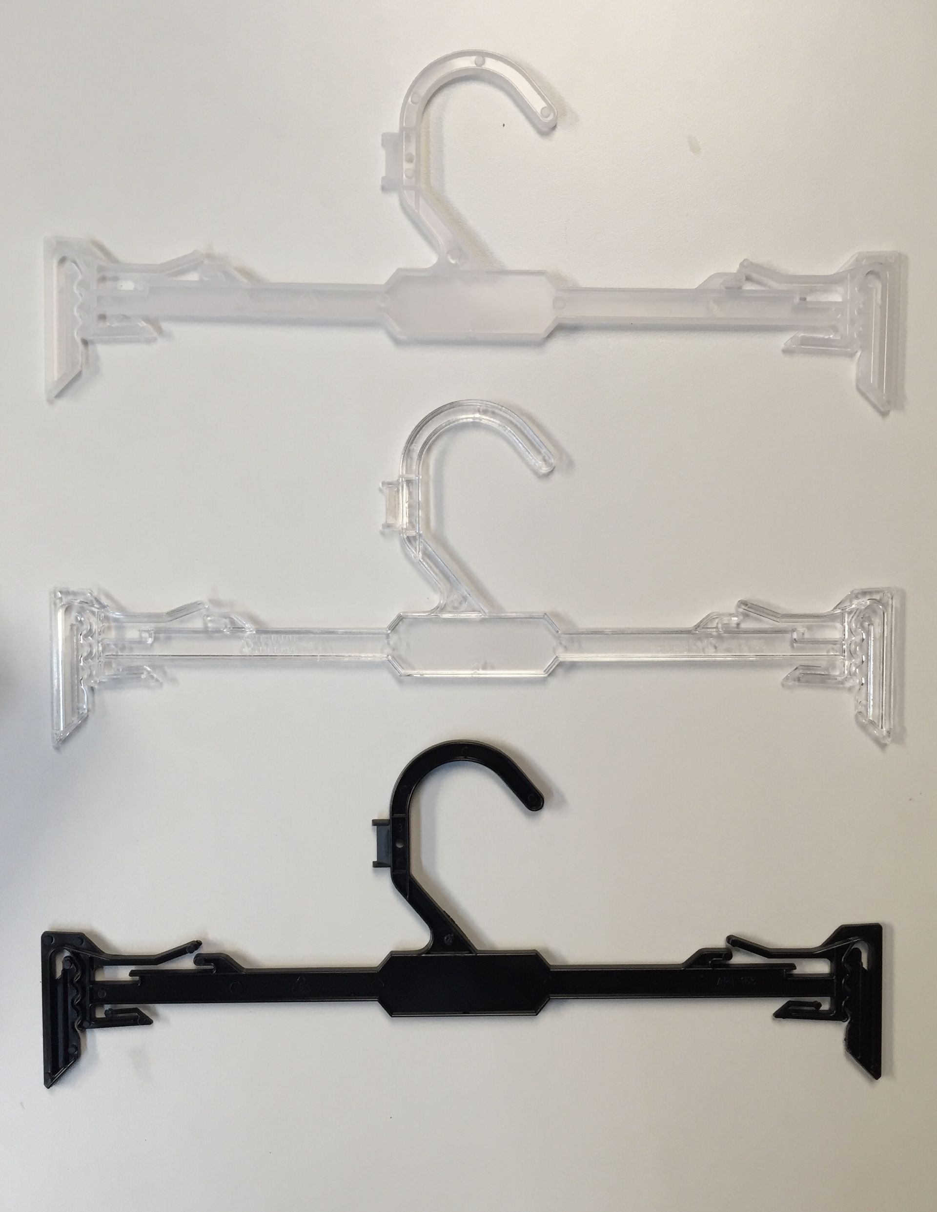 Tres perchas de plástico para pantalones: dos transparentes y una negra.