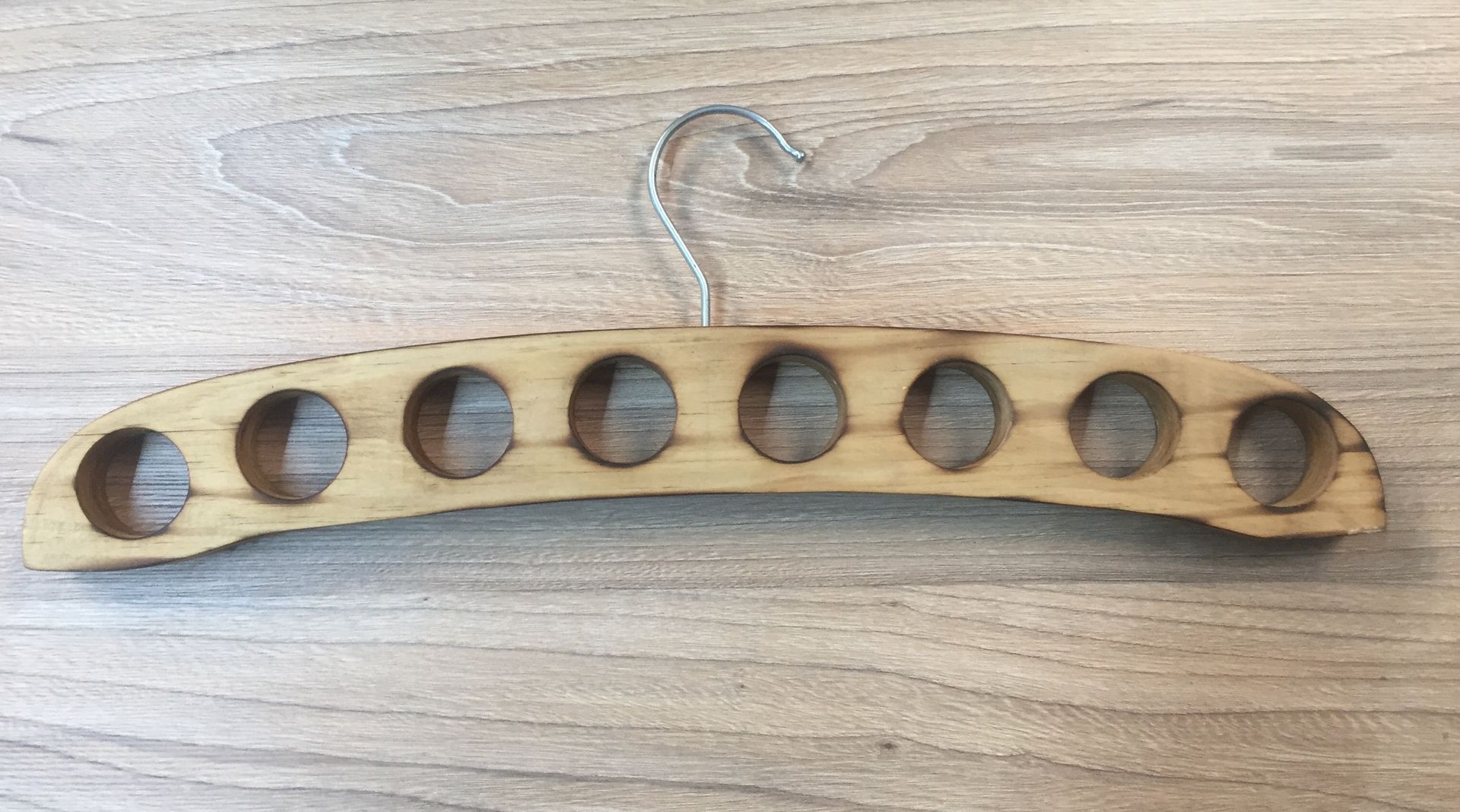Percha de madera para bufandas con múltiples aberturas circulares, gancho de metal, sobre superficie de veta de madera.