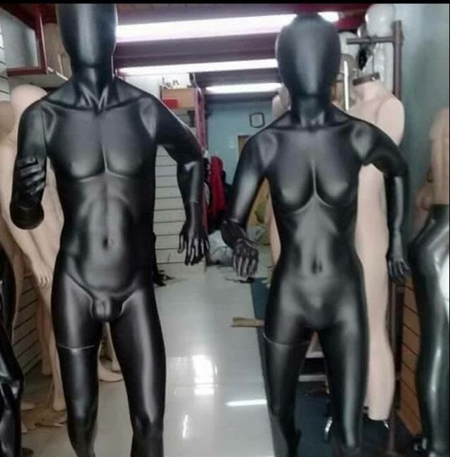 Dos maniquíes negros y brillantes, uno masculino y otro femenino, posando en posturas atléticas en una tienda.