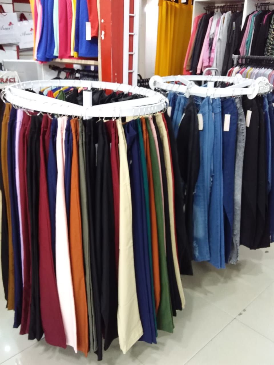 Exhibición de tienda de ropa con estantes circulares de pantalones de colores.