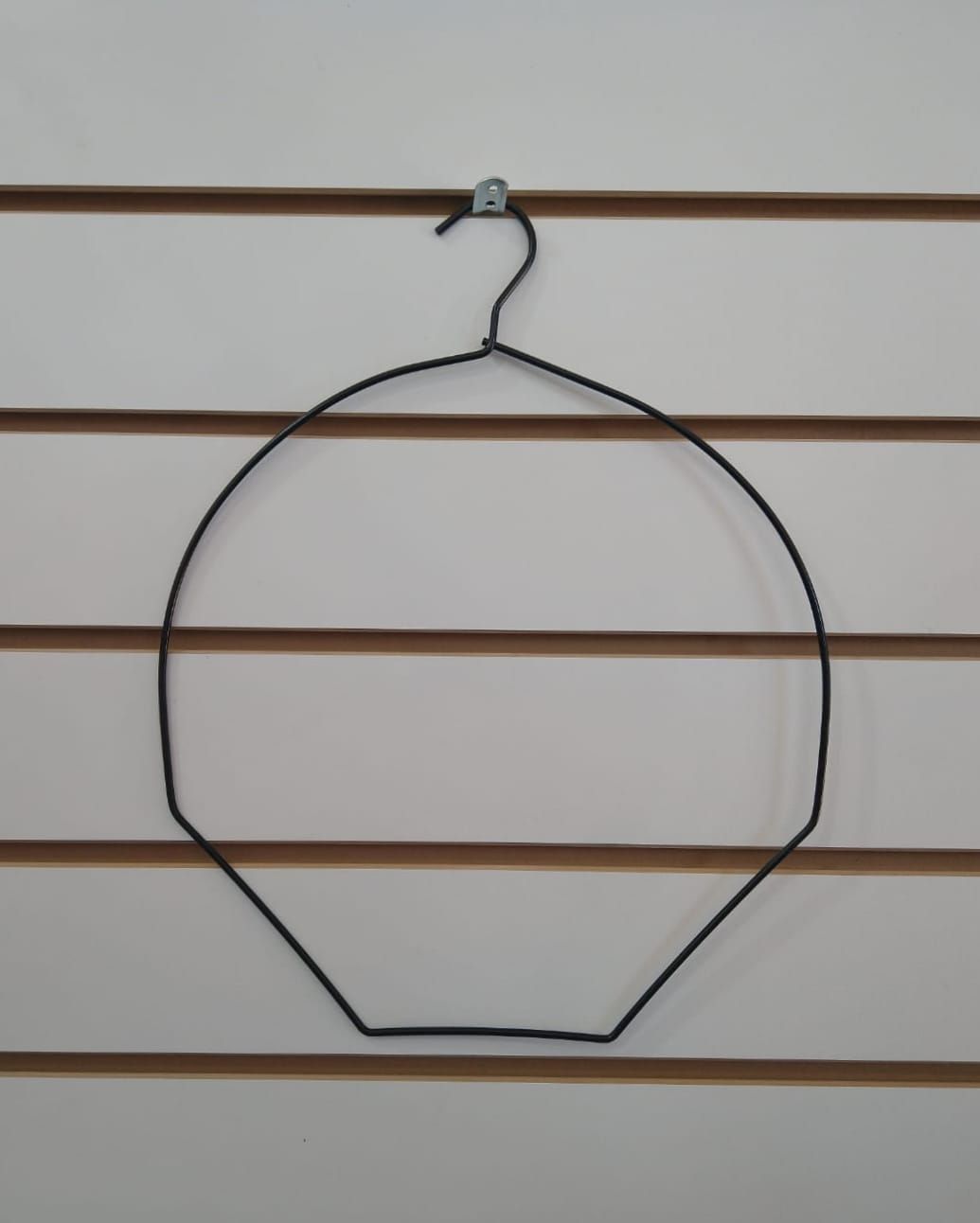 Perchero de alambre negro para sombreros sobre una pared blanca con rayas marrones horizontales.