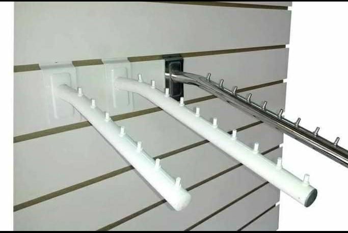 Brazos de exhibición minorista blancos con ganchos montados en una pared ranurada, que sostienen la mercancía.
