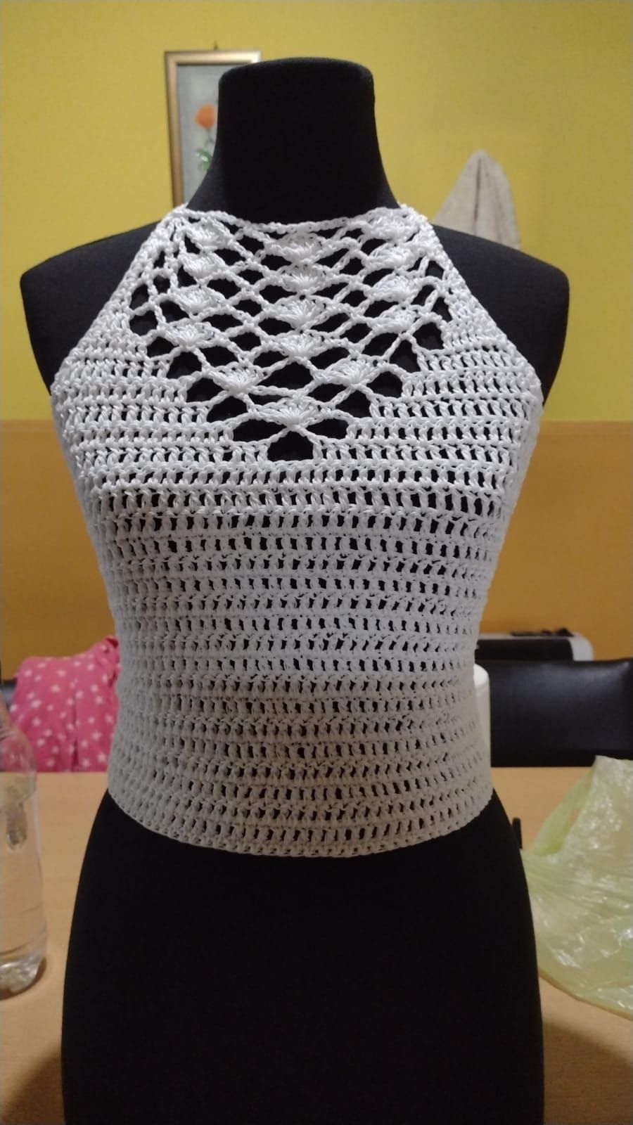 Top halter blanco tejido a crochet sobre maniquí, con escote calado y diseño de cuerpo sencillo.