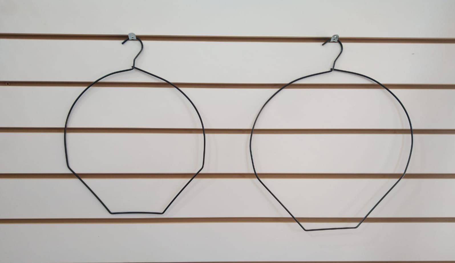 Dos expositores de sombreros con forma de alambre negro colgados en una pared blanca con rayas horizontales.