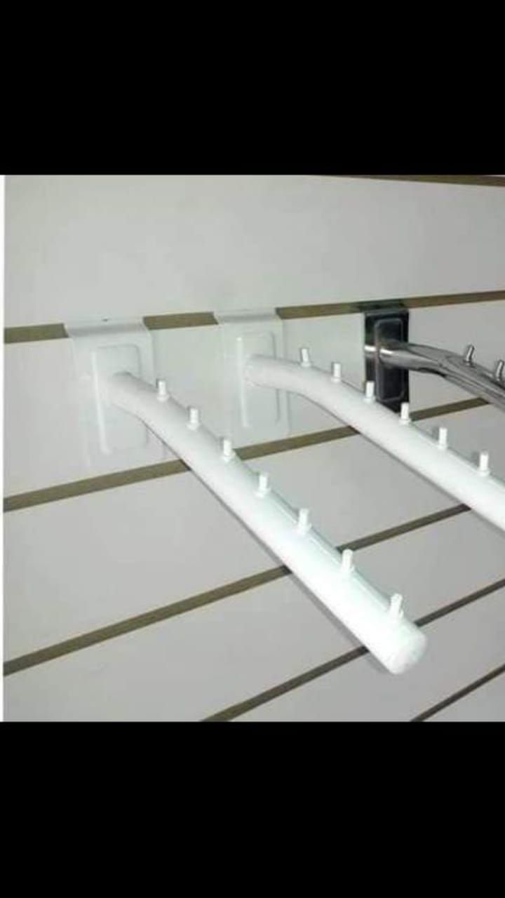 Ganchos blancos para exhibición minorista en pared ranurada, que sostienen perchas de ropa.