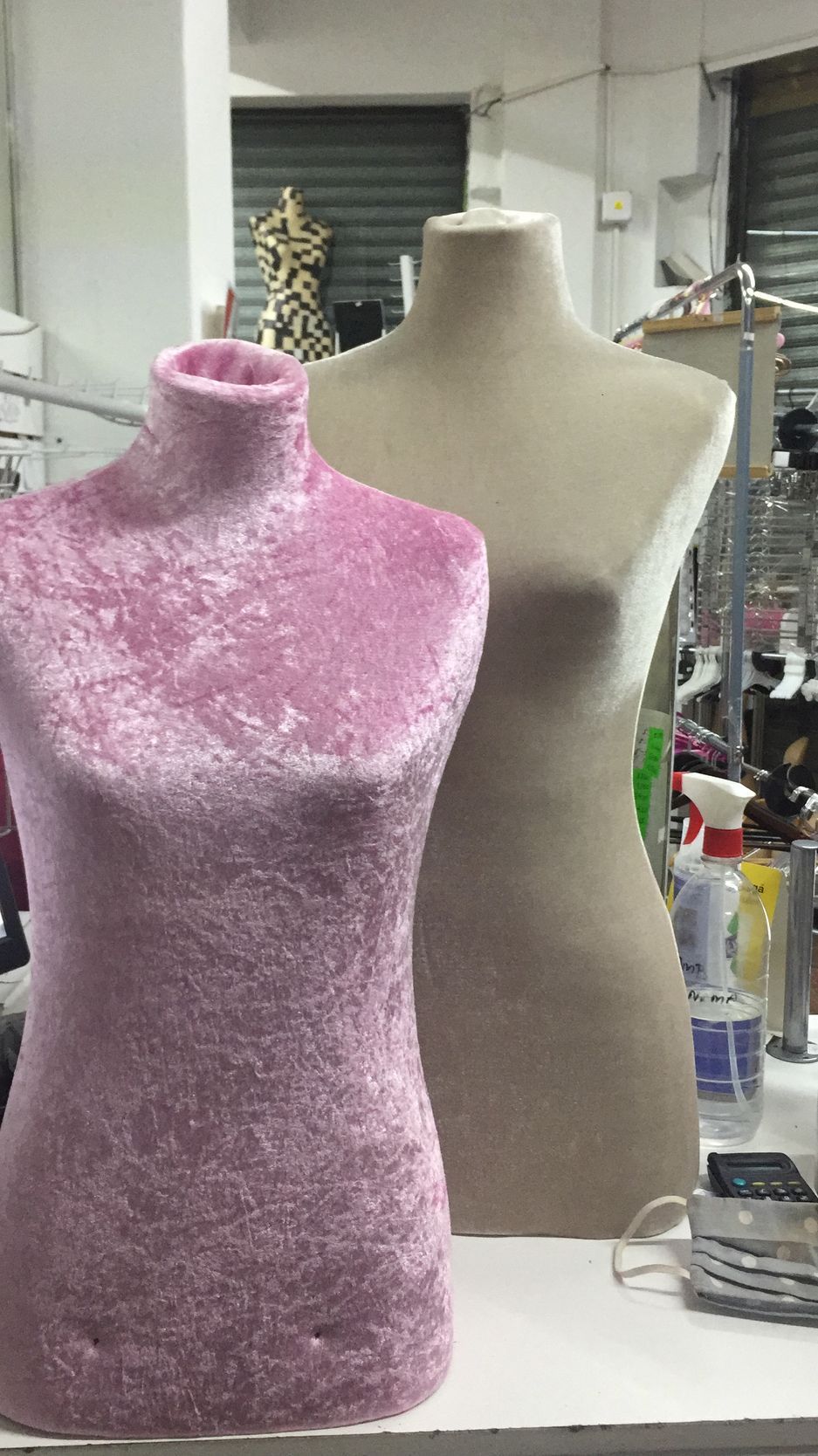 Dos maniquíes de modista en terciopelo: uno rosa y otro color canela, en un entorno de taller.