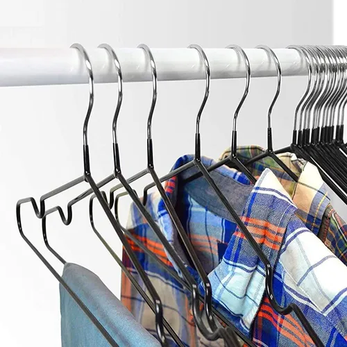 Perchas de metal negro que sostienen camisas en una barra blanca.