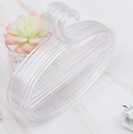 Pila de perchas de plástico transparente junto a una suculenta en maceta y una flor decorativa.