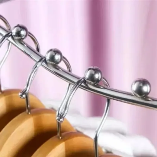 Perchero de metal plateado con perchas de madera. Fondo de tela rosa.