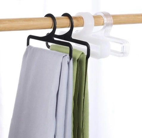 Tres perchas que sostienen bufandas grises y verdes, colgando de una varilla de madera.