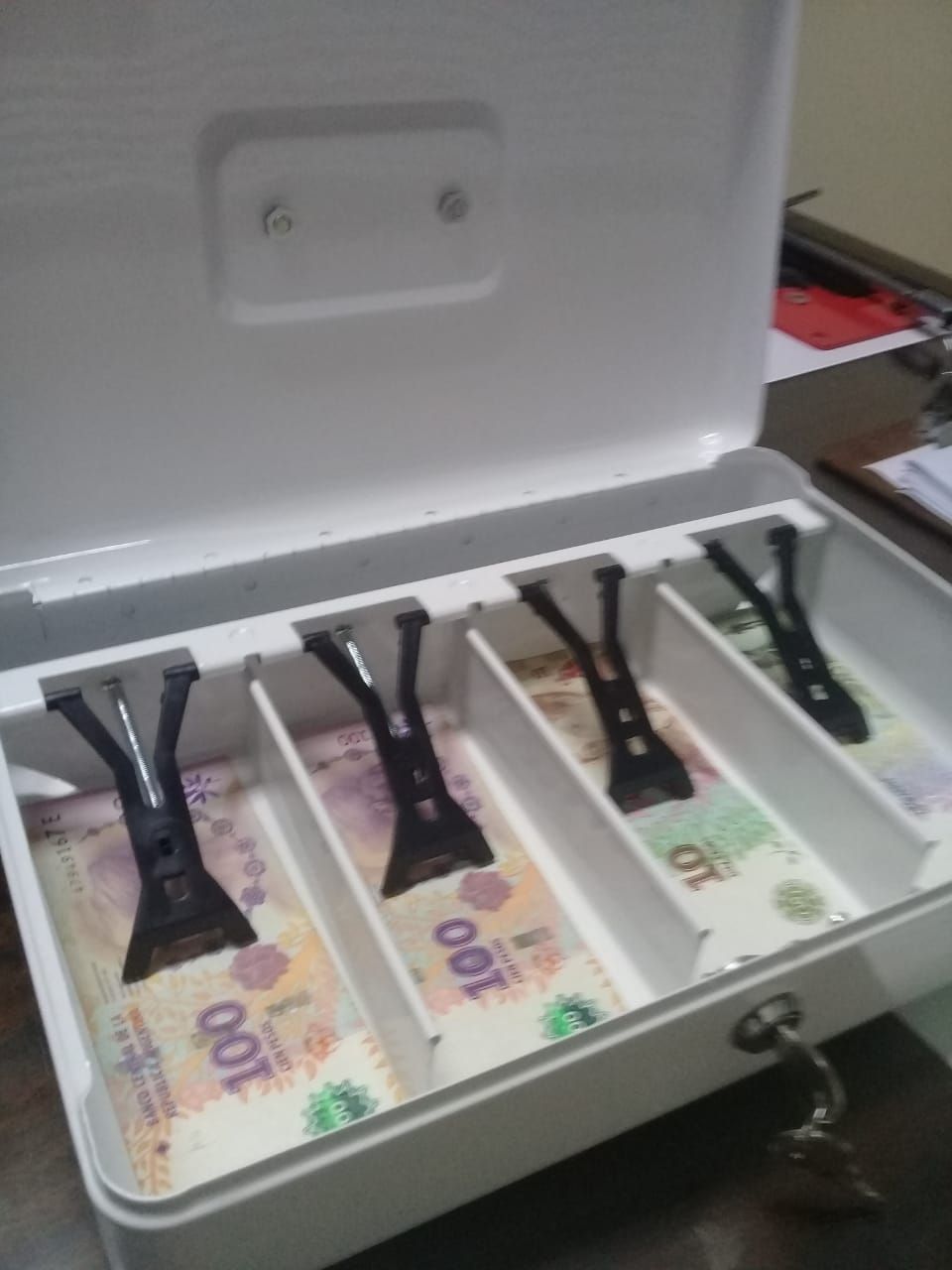 Caja blanca abierta que contiene billetes de 100 pesos argentinos en ranuras separadas.