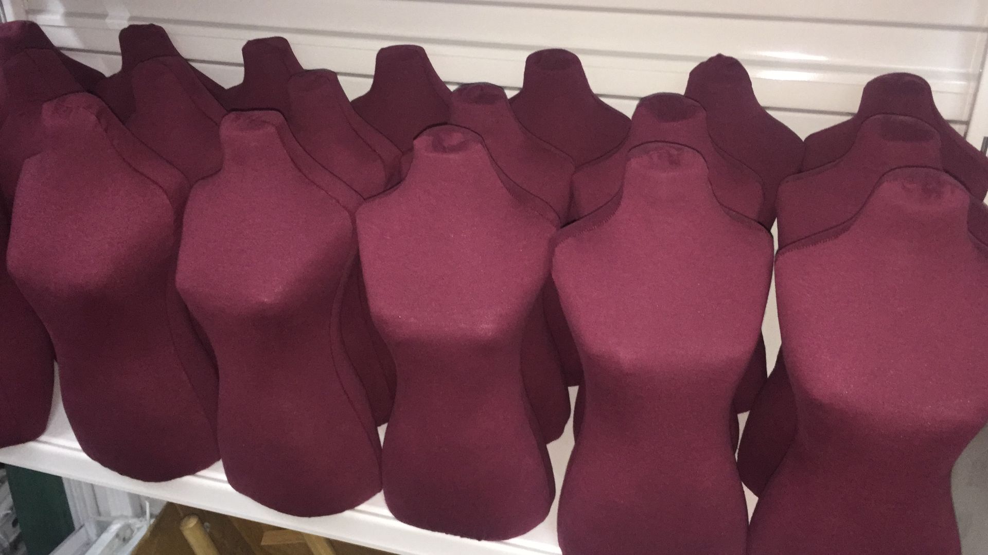 Filas de bustos exhibidos en forma de collar de color granate sobre un estante blanco.