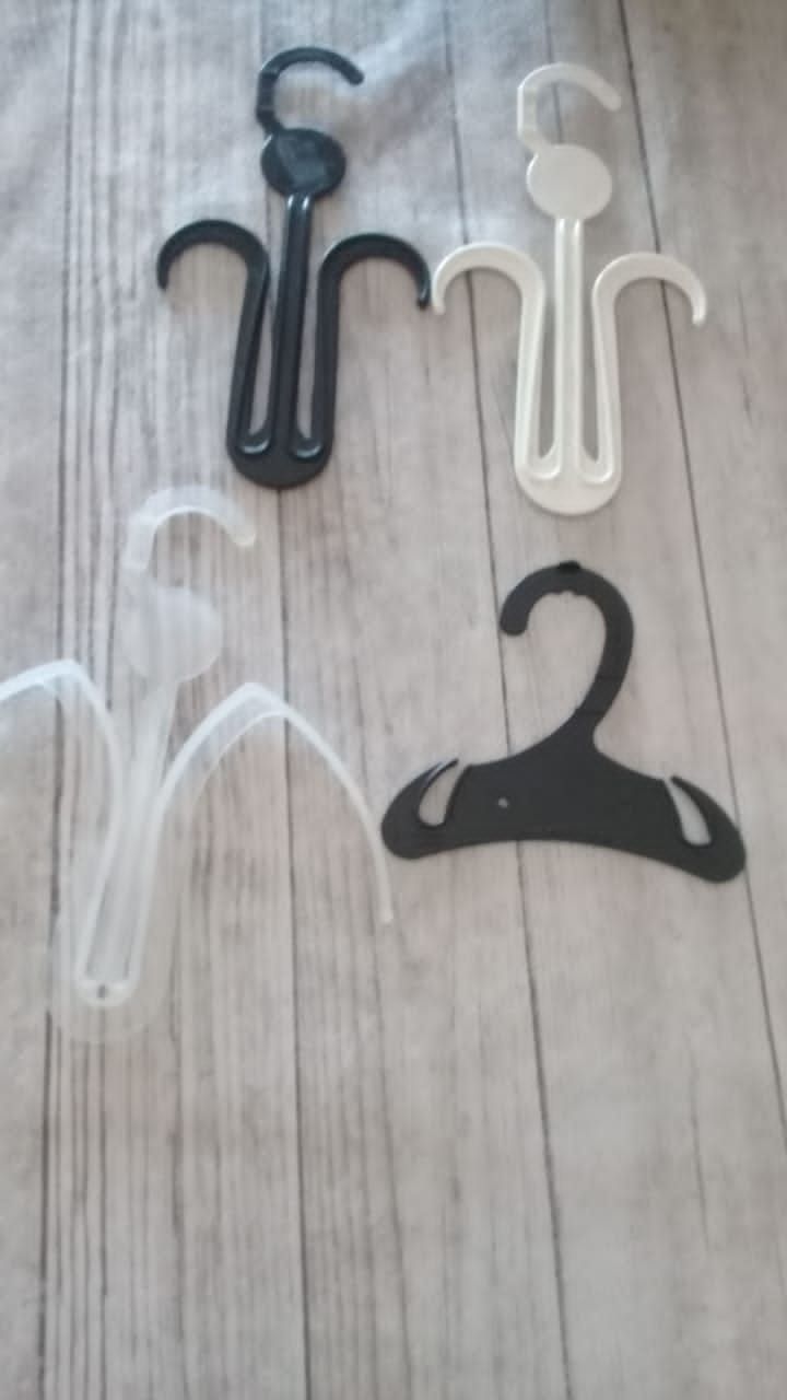 Cuatro perchas de plástico para ropa, dos negras y dos blancas, dispuestas sobre una superficie de madera clara.