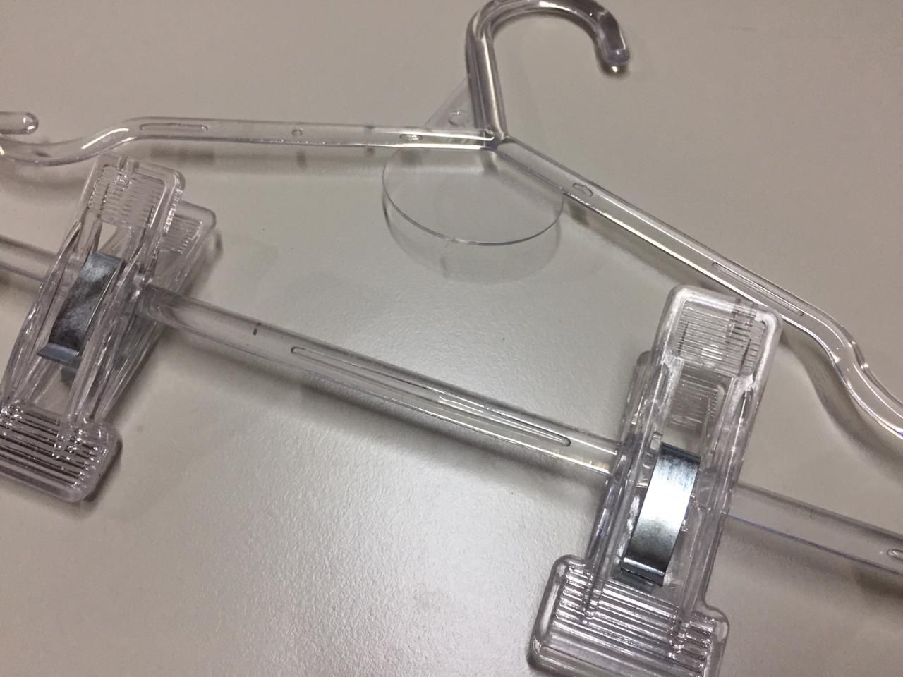 Percha de ropa de plástico transparente con pinzas, apoyada sobre una superficie clara.