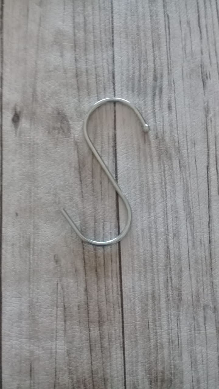 Gancho en forma de S de metal plateado sobre una superficie de veta de madera gris claro.