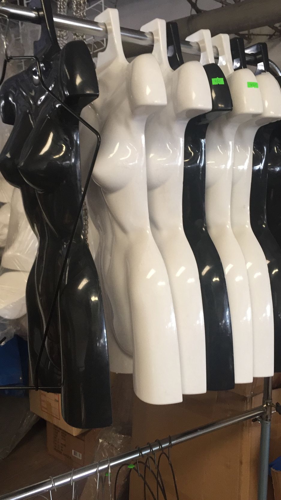 Maniquíes de torso femenino en blanco y negro colgados en un estante de metal.