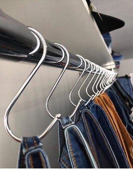 Vaqueros colgados de ganchos con forma de S en una barra plateada en un armario.