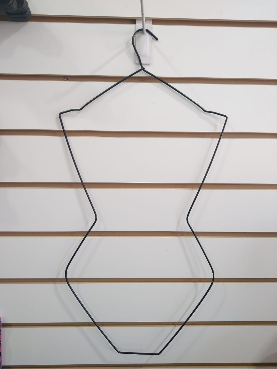 Percha de alambre negro para maniquí que cuelga de una pared con listones blancos y marrones.