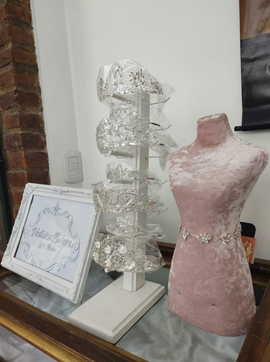 Exhibición de tiaras de novia en un soporte giratorio y un maniquí rosa con un cinturón adornado con joyas.