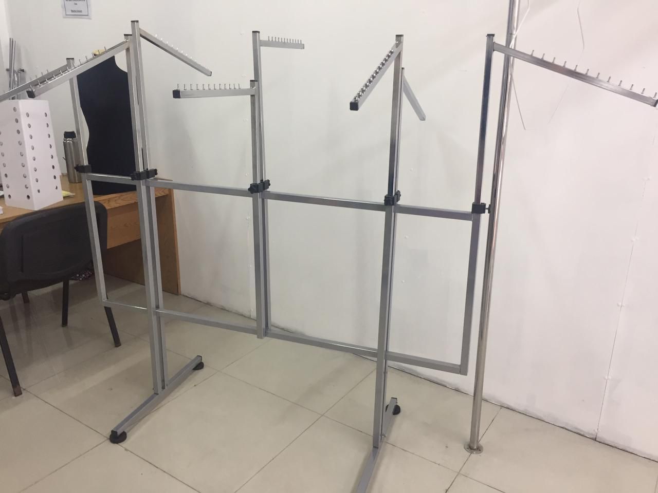 Percheros de ropa hechos de metal en una habitación vacía, apoyados contra una pared y un suelo blancos.