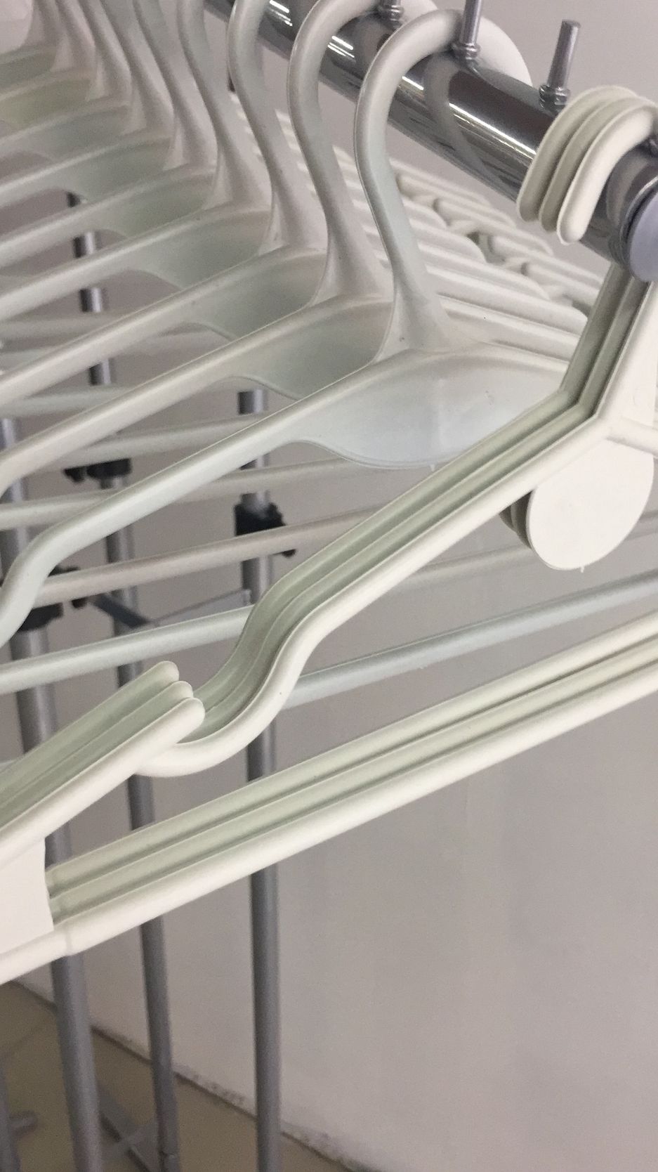 Perchas de plástico blanco sobre un estante de metal plateado, primer plano, en una habitación luminosa.