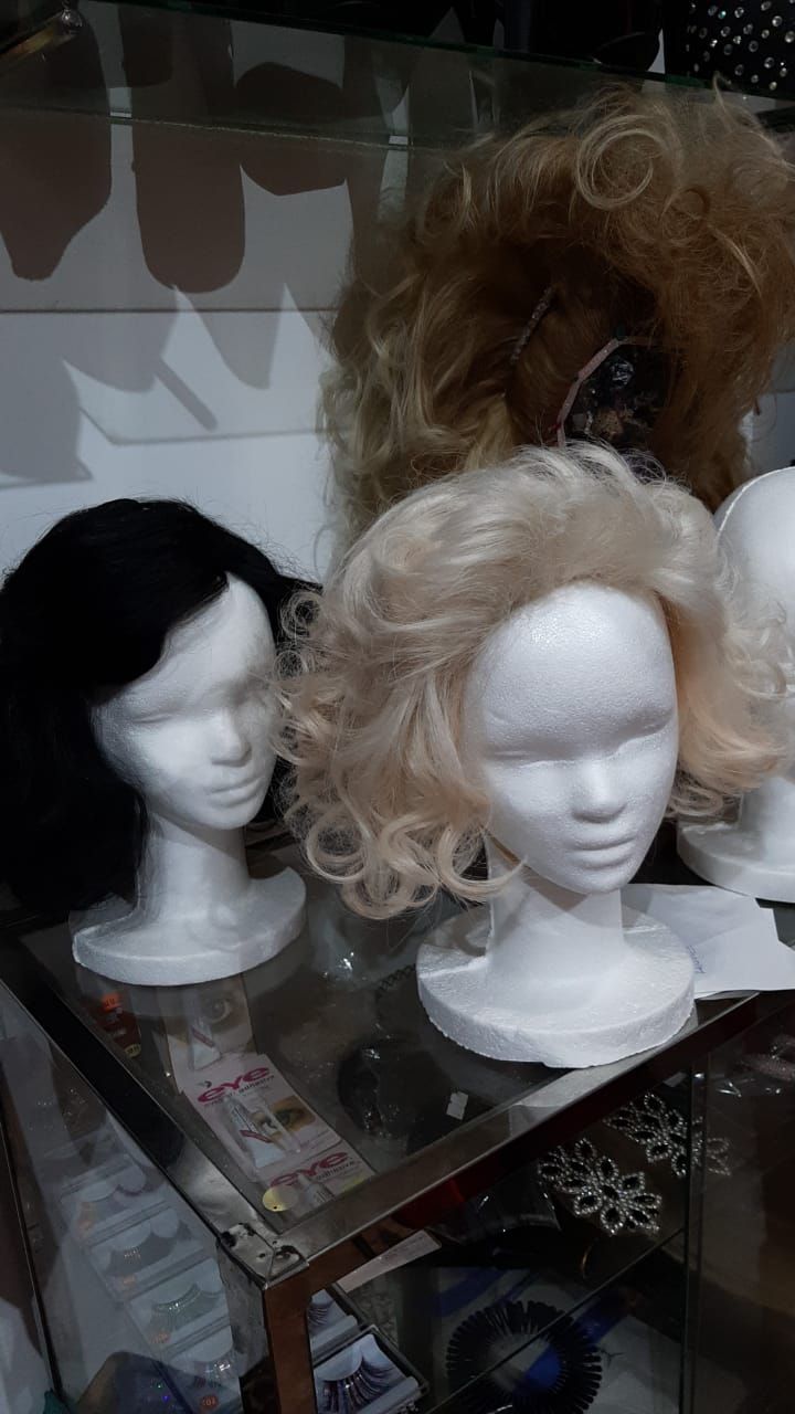 Pelucas sobre cabezas de maniquí de espuma exhibidas en un estante de vidrio; colores negro, rubio y castaño claro.