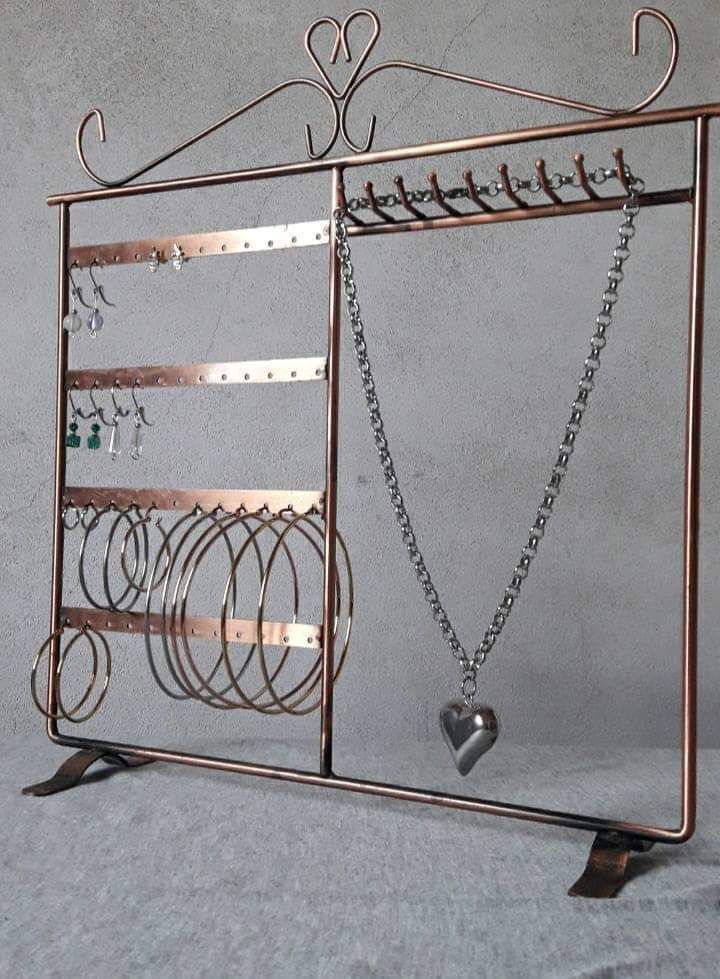 Organizador de joyas de metal de color cobre que contiene aretes, pulseras y un collar con colgante de corazón.