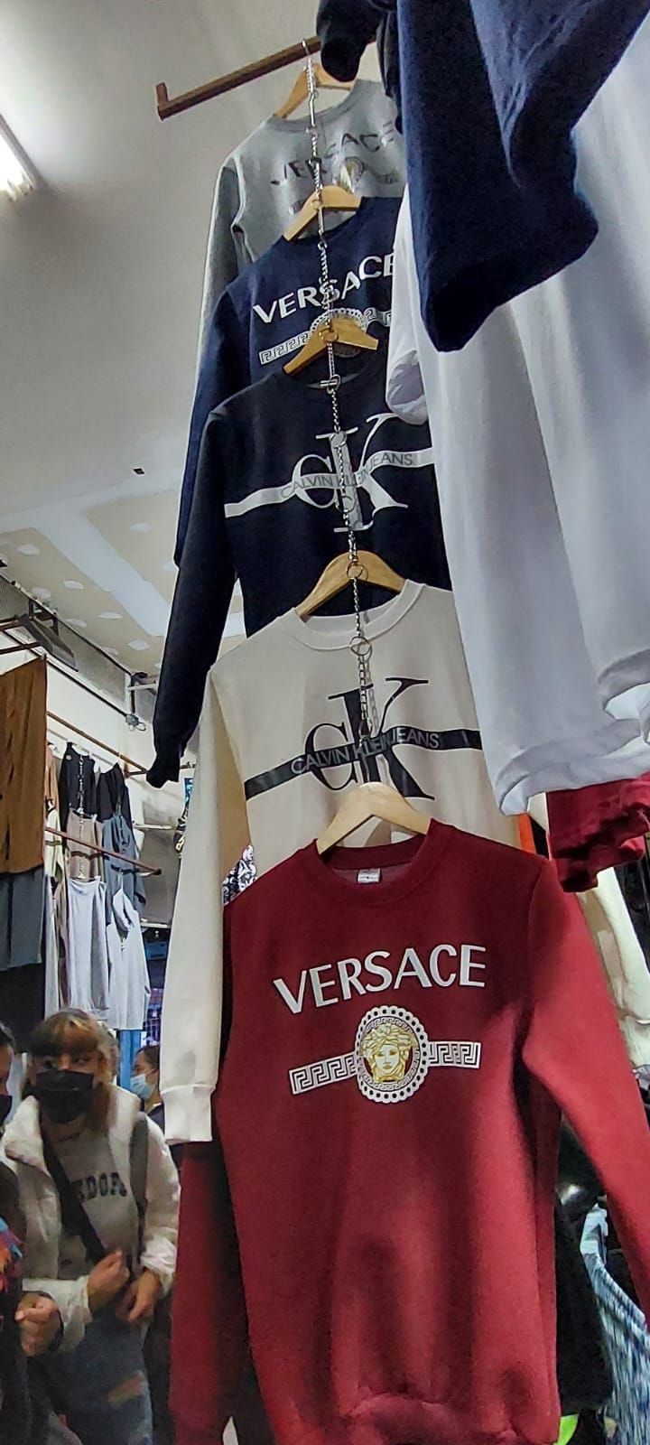 Perchero con sudaderas Versace de varios colores. En primer plano, una persona con mascarilla.