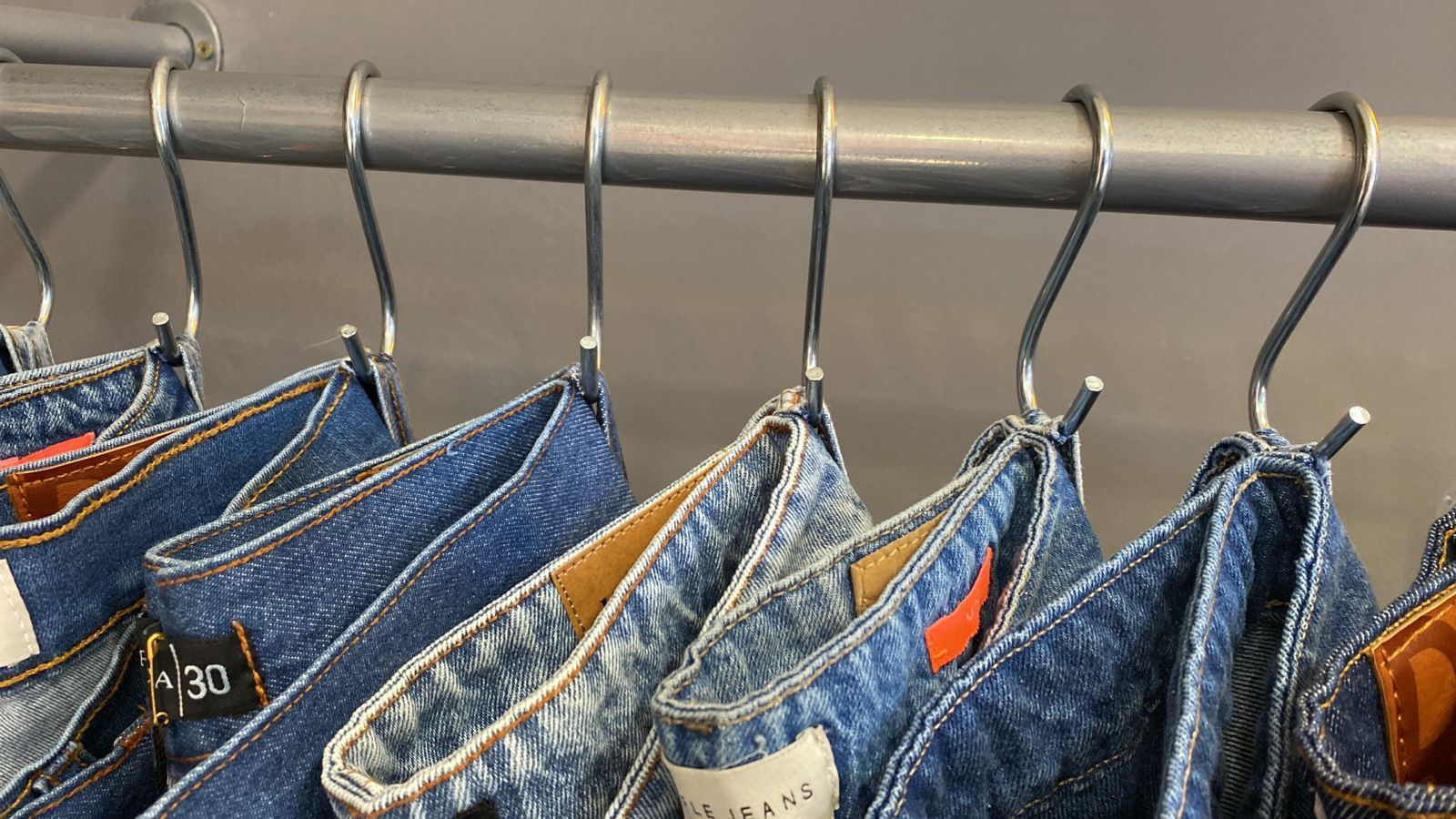 Pantalones vaqueros azules colgados de una barra de metal con ganchos metálicos en forma de S.