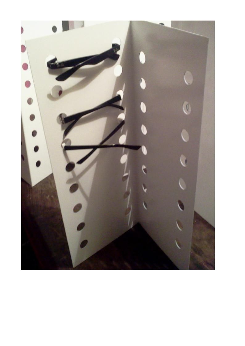 Expositor de papel blanco con bandas elásticas negras colocadas entre agujeros para sujetar los artículos.